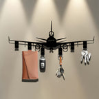 Airplane Key Holder mounted on a taupe wall beneath spotlights, with keyrings and a tan pouch hanging below.