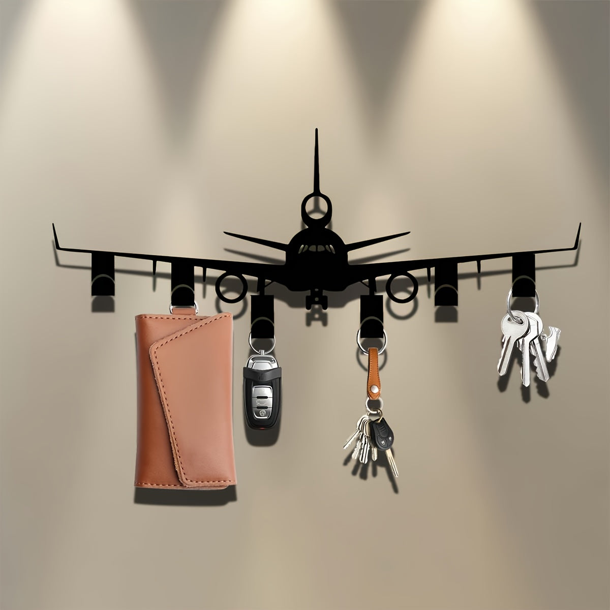 Airplane Key Holder mounted on a taupe wall beneath spotlights, with keyrings and a tan pouch hanging below.