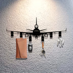 Airplane Key Holder in black metal on a textured white wall, holding keys, a car fob, and a tan pouch.