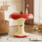 Apple Bite Side Table holding books and a slim vase beside a tan armchair