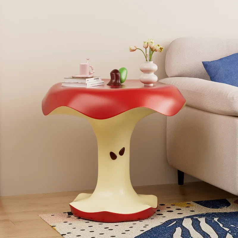 Red apple-core side table with green leaf detail beside a cream sofa