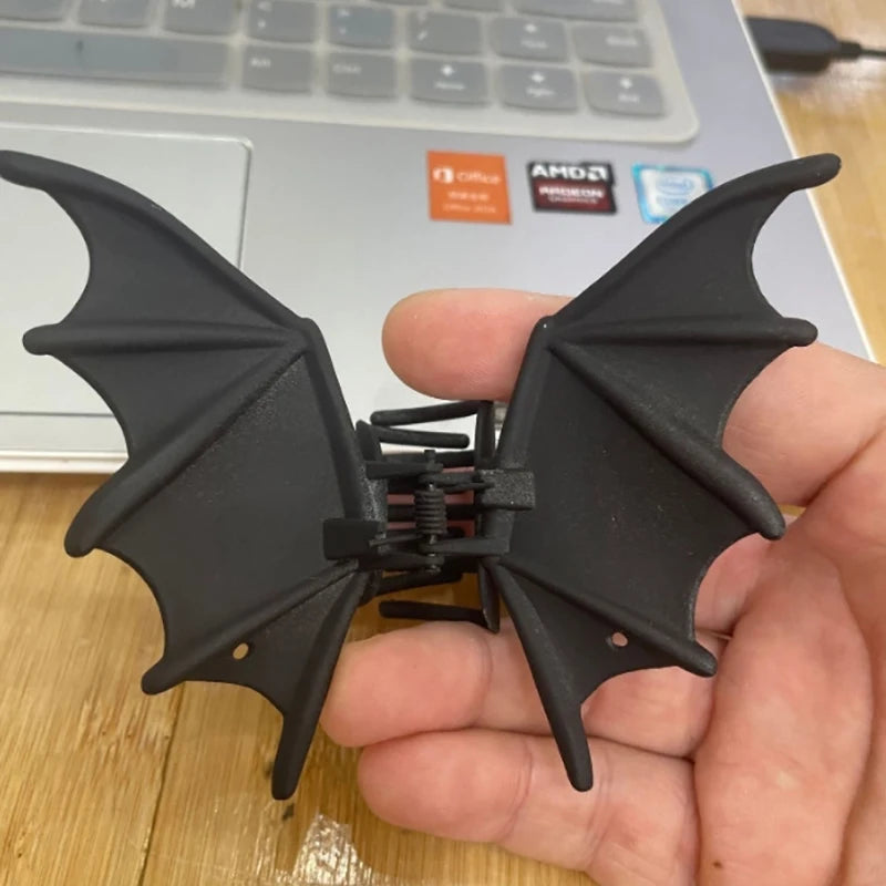 Bat Wing Claw Clip resting in a hand beside a laptop, showing the black wing details.