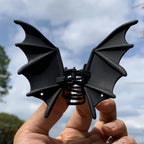 Bat Wing Claw Clip held against the sky, showing sculpted black wings and the central spring.