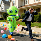 Big-Head Inflatable Alien Costume beside a running man on a neighborhood street scattered with balloons.