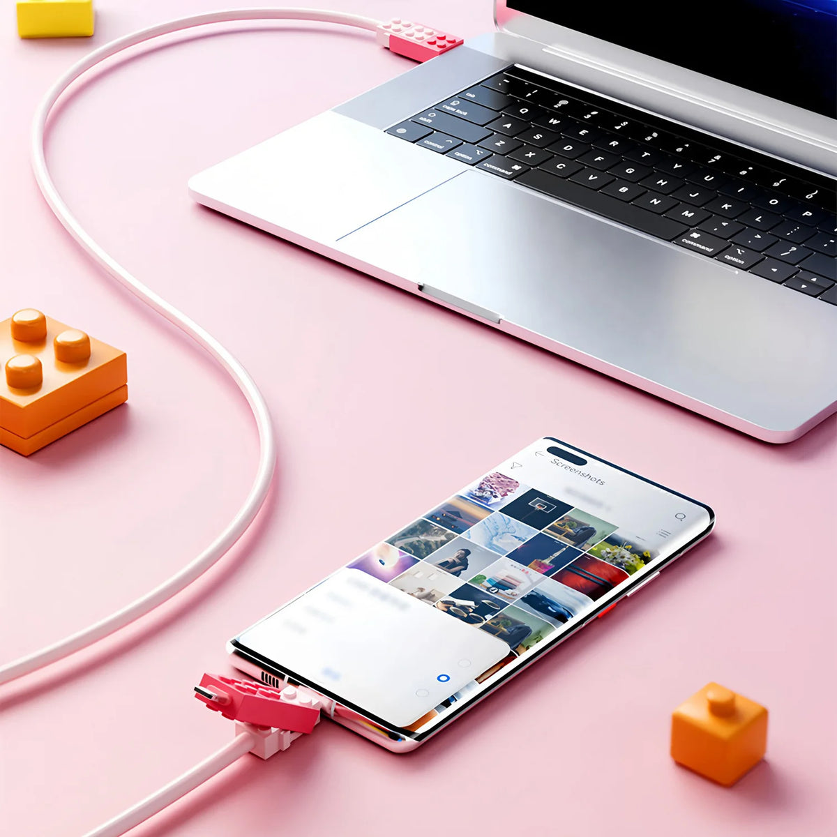 Building Block Charging Cable in pink pictured with a phone and laptop on a pink desk