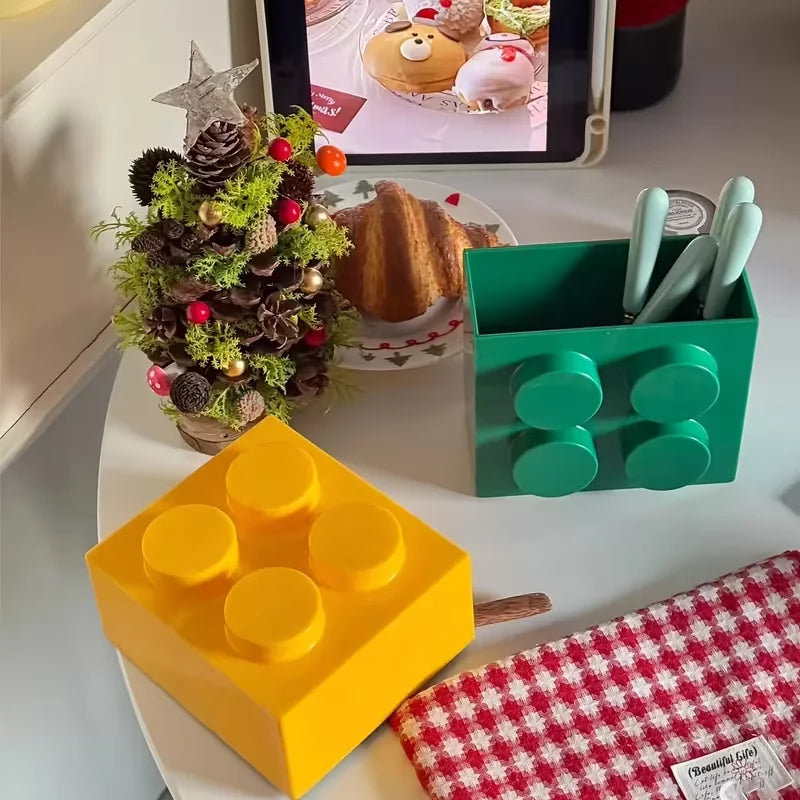 Building Block Storage Bins — Green utensil bin and yellow bin shown on a counter beside festive decor.