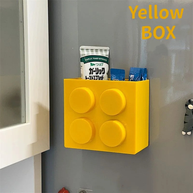 Building Block Storage Bins — Yellow bin storing small packets and a tube on a gray refrigerator.