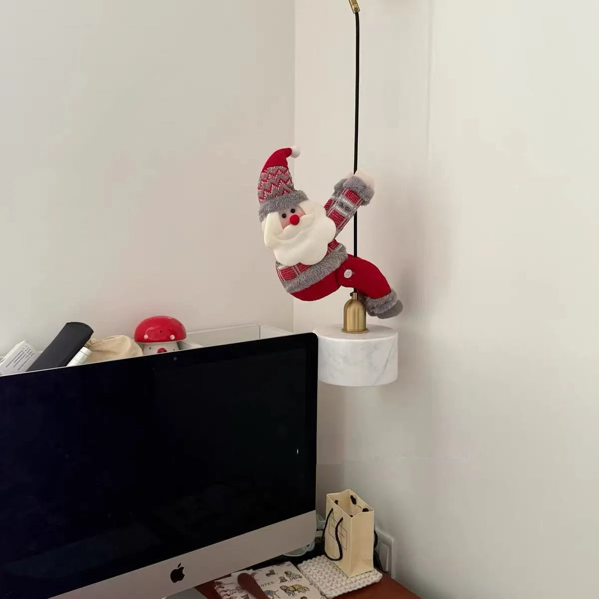 Christmas Chandelier Hugger Santa character hanging from a cord above a home office monitor