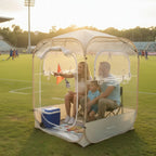Clear View Bubble Tent with two adults and a child seated beside a soccer field at sunset.