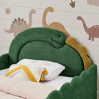 Close-up of green bouclé dinosaur headboard with smiling face and yellow accent