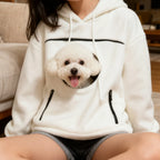Cozy Pet Carrier Hoodie in white worn while seated indoors with a fluffy dog in the front pouch