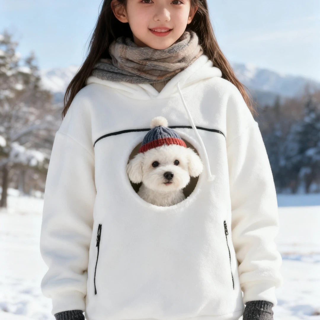 Cozy Pet Carrier Hoodie in white carrying a dog wearing a knit hat against a snowy mountain background