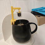 Crane Tea Bag Holder on a black mug, holding the tea tag and string while the bag steeps inside.