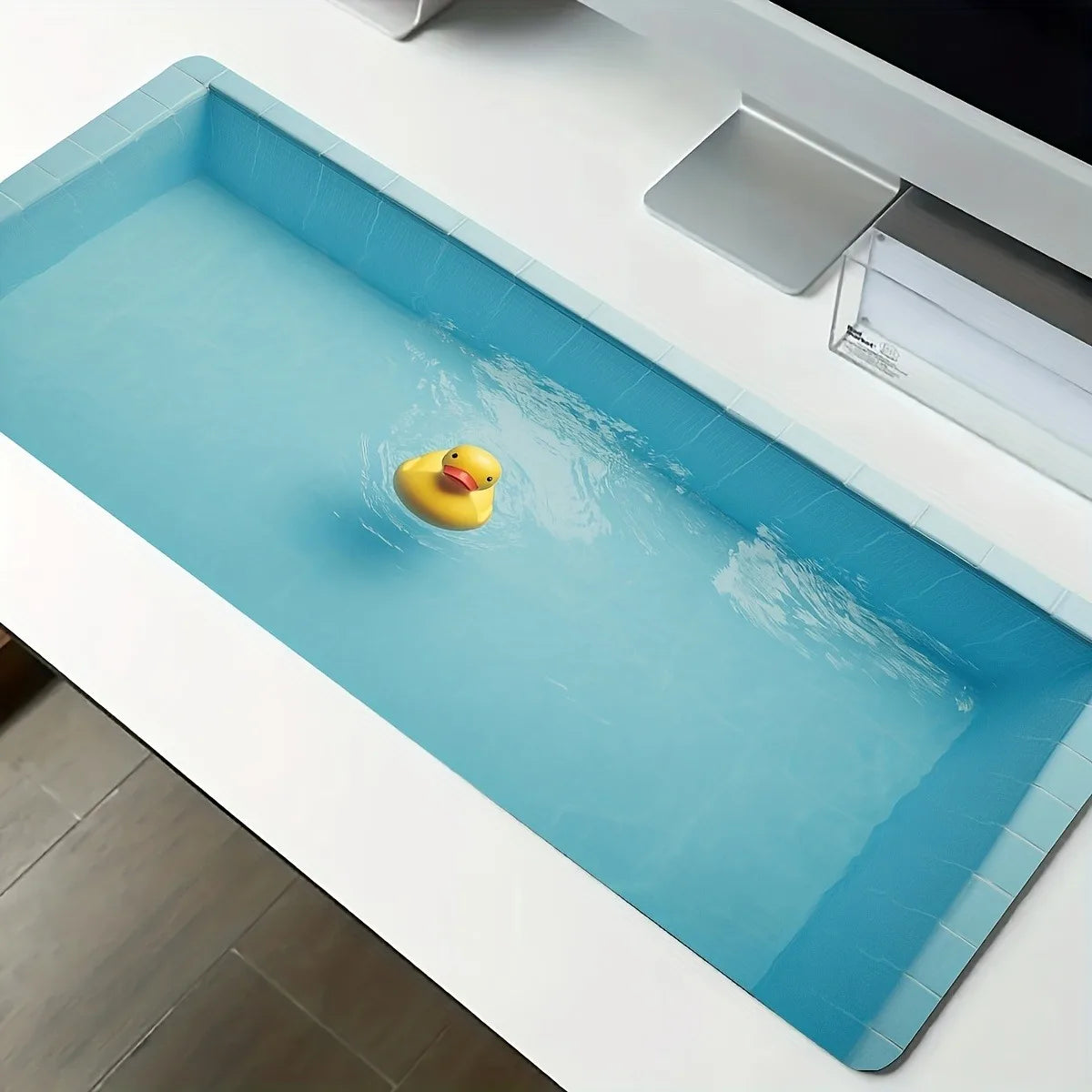 Cute Duck Desk Mat angled view of the printed yellow duck, blue water and tiled border on a white desk