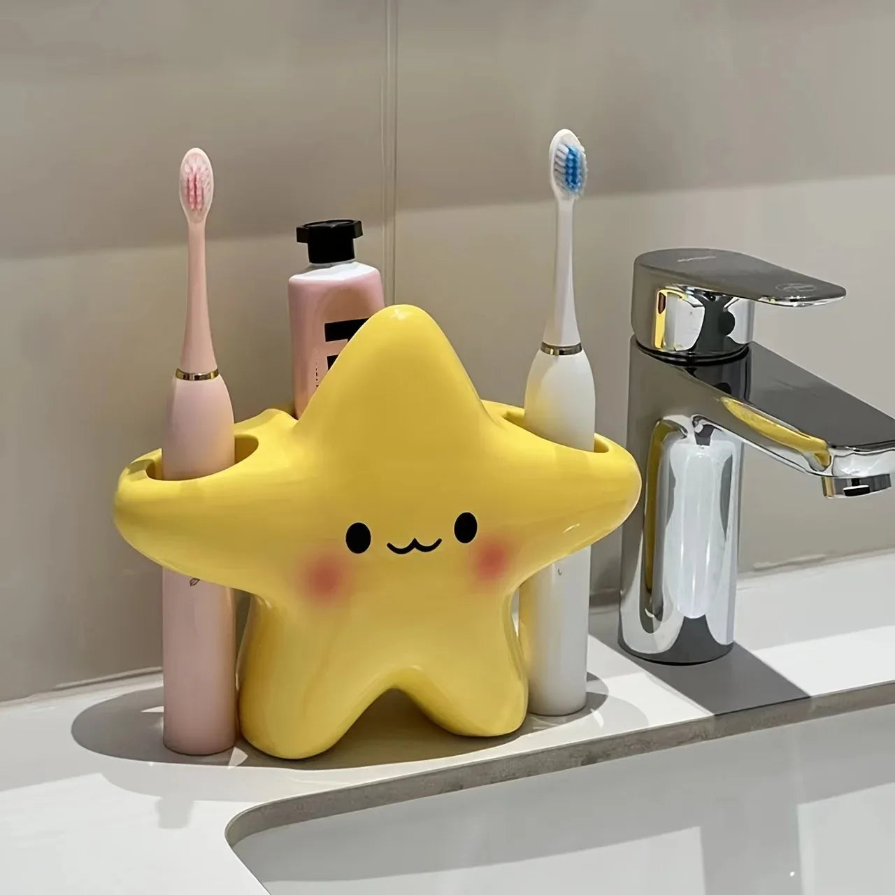 Cute Star Toothbrush Holder beside a chrome faucet with two electric toothbrushes and toothpaste stored upright
