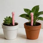 Cute Worm Plant Ornaments: two pink worms beside a succulent and a leafy plant in white and terracotta pots.