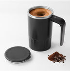Digital Self-Stirring Mug open black mug with matching lid and coffee beans arranged beside it on a pale background.