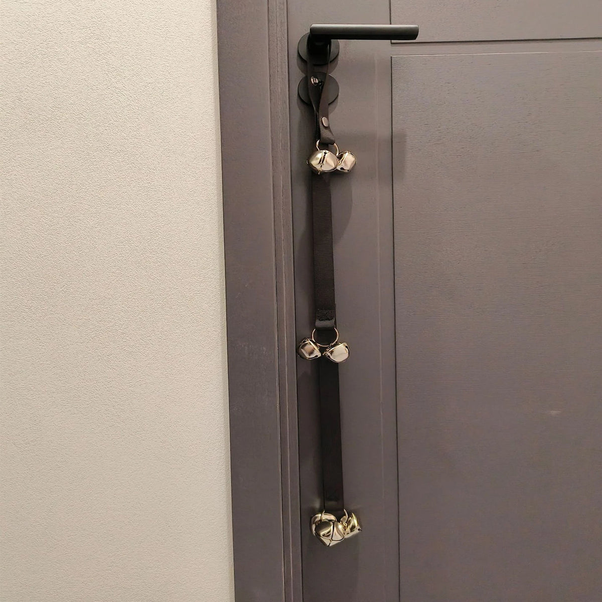 Black nylon dog potty training bells hanging from a dark door handle