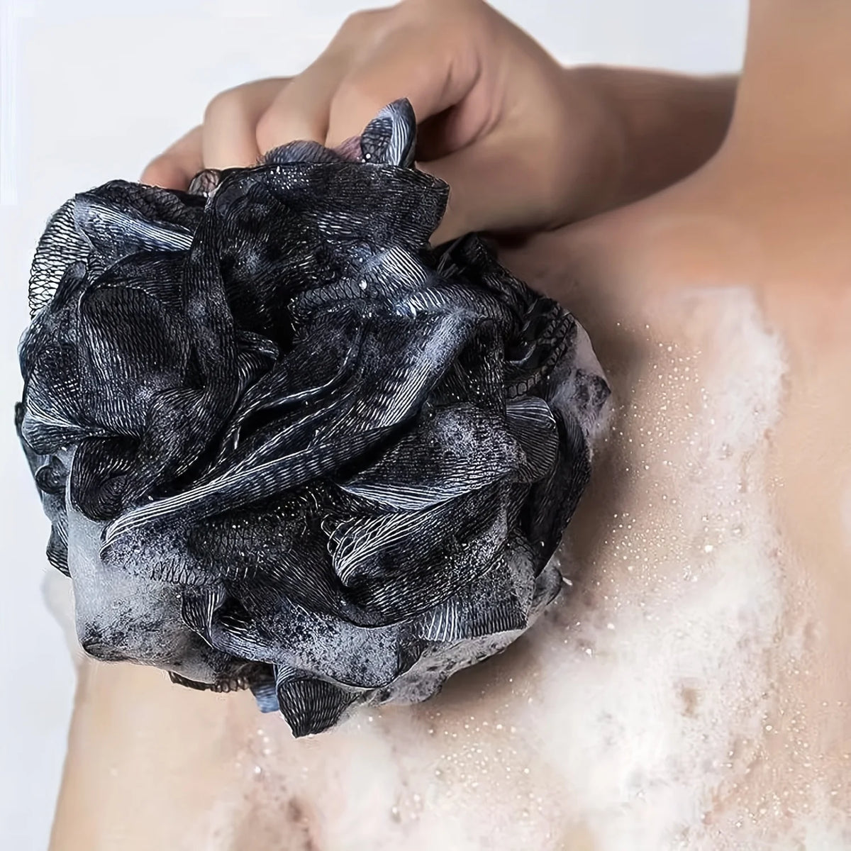 Black mesh shower loofah held against a shoulder with soap lather