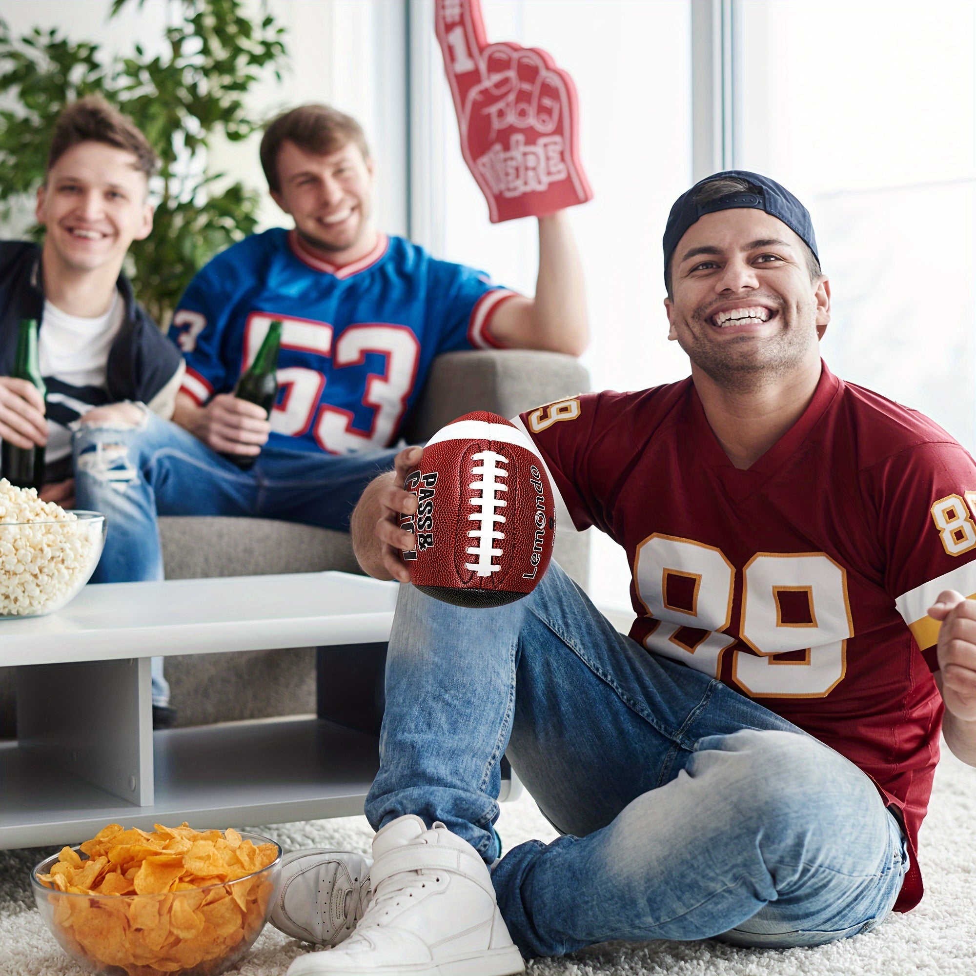 GripEgg™ Trainer – PASS & CATCH Edition in red with white laces held by man in football jersey, casual living room setting, HighPeak