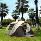Family Pop-Up Tent brown model in a palm-lined park, showing its left mesh window and open front doorway.