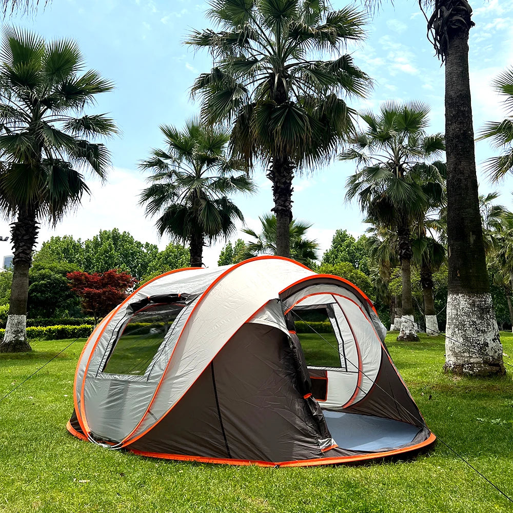 Family Pop-Up Tent brown model in a palm-lined park, showing its left mesh window and open front doorway.