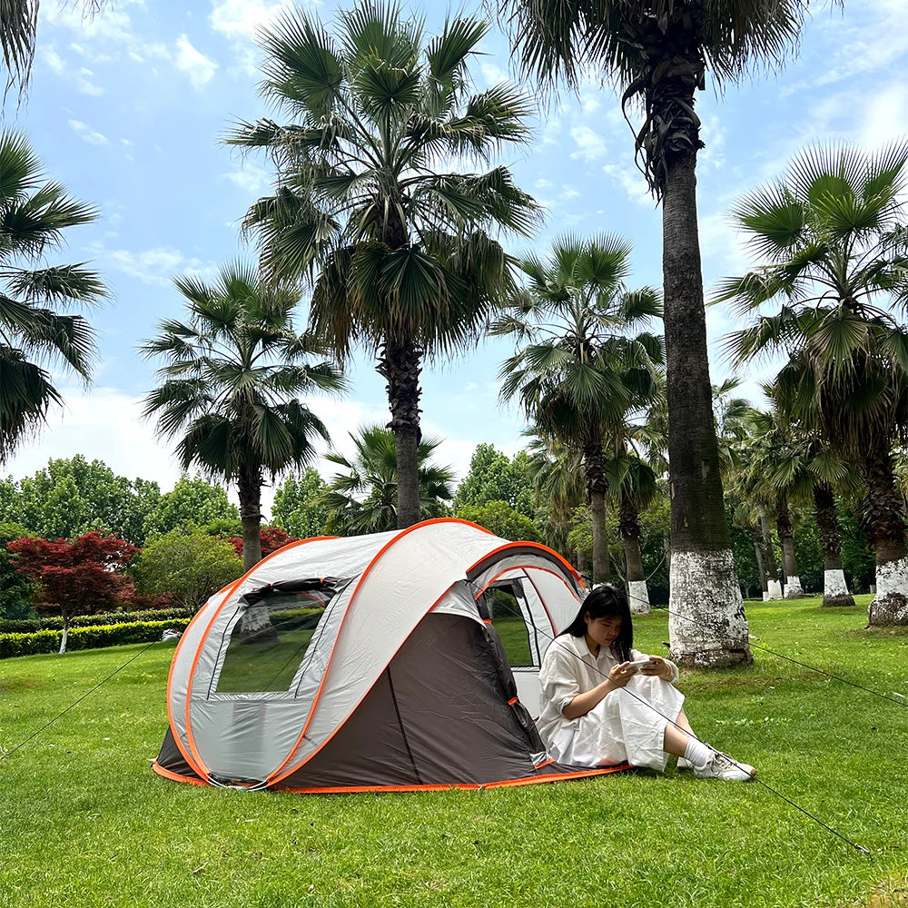 Family Pop-Up Tent in brown and gray with a camper seated at the doorway beneath palm trees.
