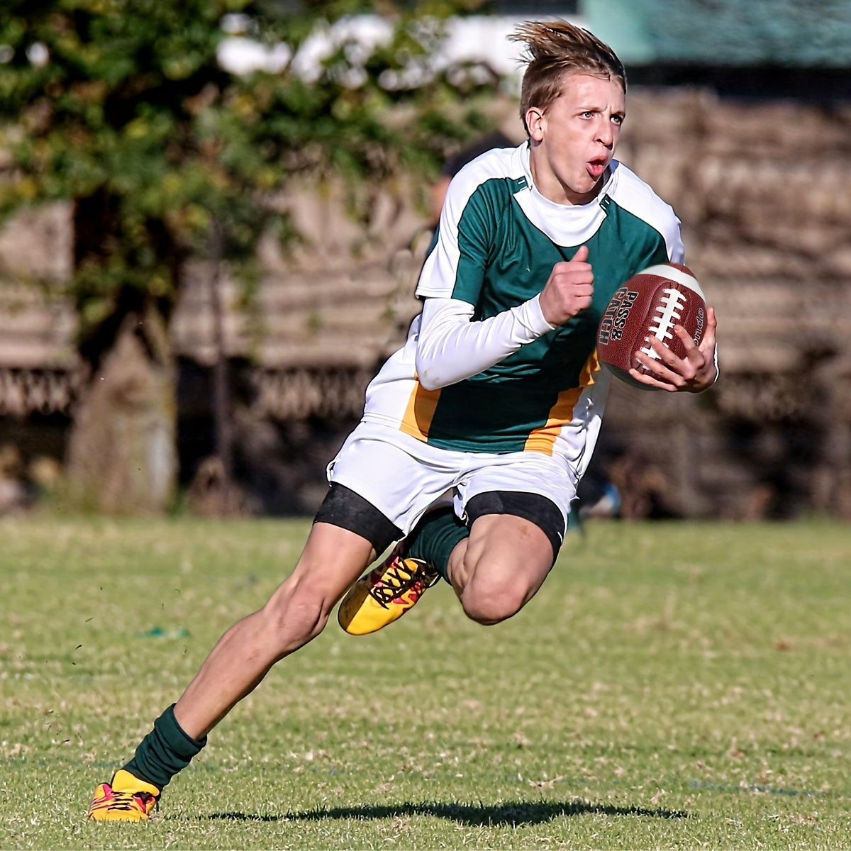 GripEgg™ Trainer – PASS & CATCH Edition held by young football player running on green field in bright sunlight