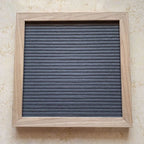 Felt Letter Board in gray mounted vertically on a wall inside its natural wooden frame.