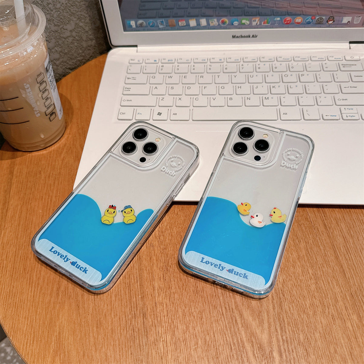 Floating Ducks Phone Case both duck designs resting beside a laptop and iced drink on a wooden desk