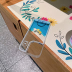 Floating Ducks Phone Case empty Three Ducks case on a floral mat, showing its transparent shell and camera cutout