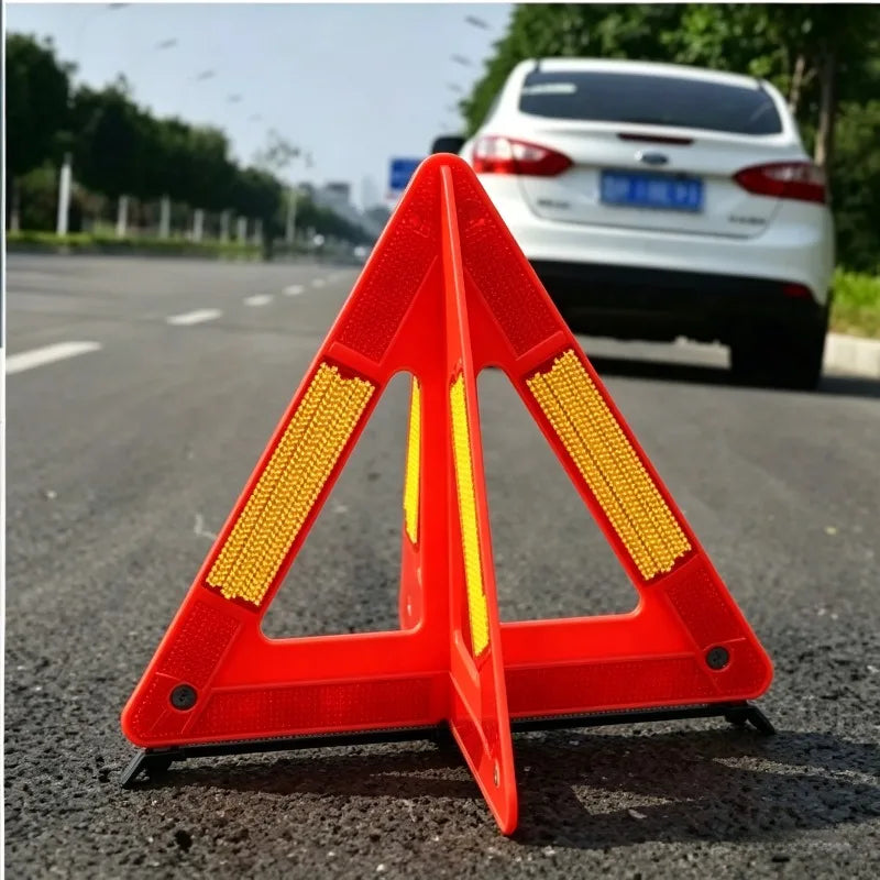 Foldable Warning Triangle close-up on asphalt behind a white parked car, showing its reflective side panels.