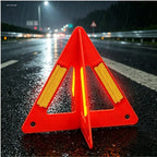 Foldable Warning Triangle shown on a rain-soaked road at night with traffic lights blurred behind it.