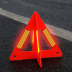 Foldable Warning Triangle standing open on dark asphalt, with a red body and bright reflective panels.
