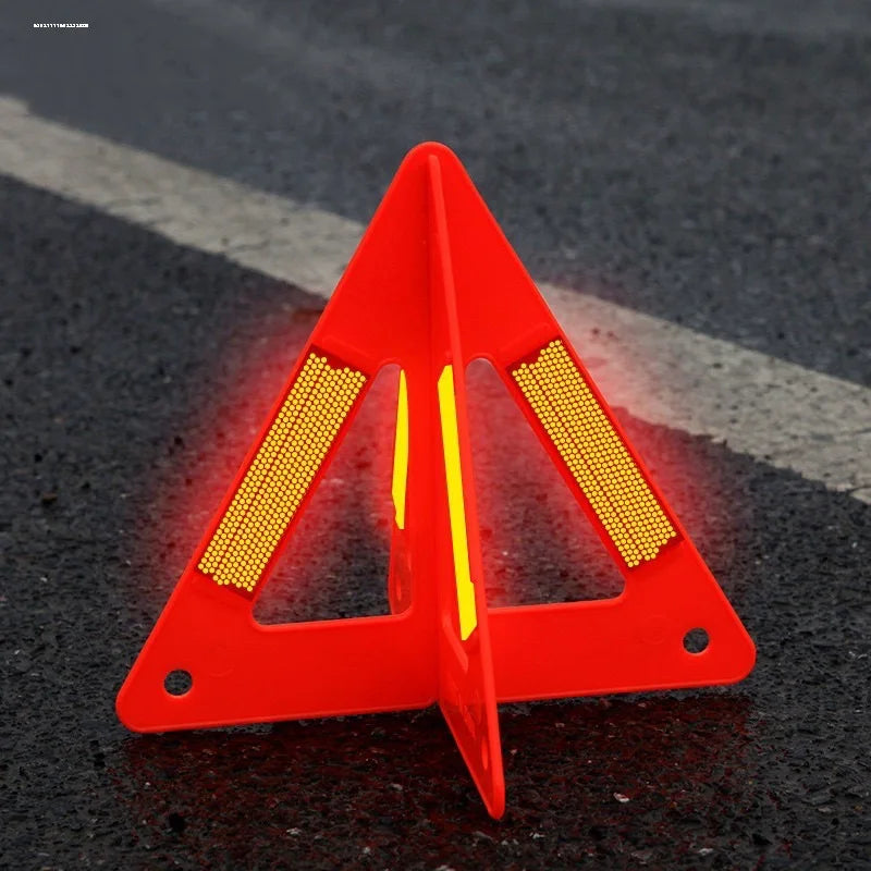 Foldable Warning Triangle standing open on dark asphalt, with a red body and bright reflective panels.
