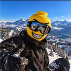 Funny Brickhead Ski Mask with white and gold teeth, worn by a snowboarder giving a thumbs-up beside a mountain lake