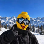 Funny Brickhead Ski Mask with a red tongue-out expression, worn with goggles against a snowy mountain backdrop