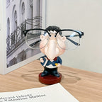 Funny Teacher Glasses Stand displaying black eyeglasses on a wooden desk beside framed wall art