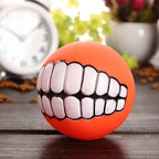 Funny Teeth Dog Balls orange ball on a wood tabletop with a clock and plants in the background.
