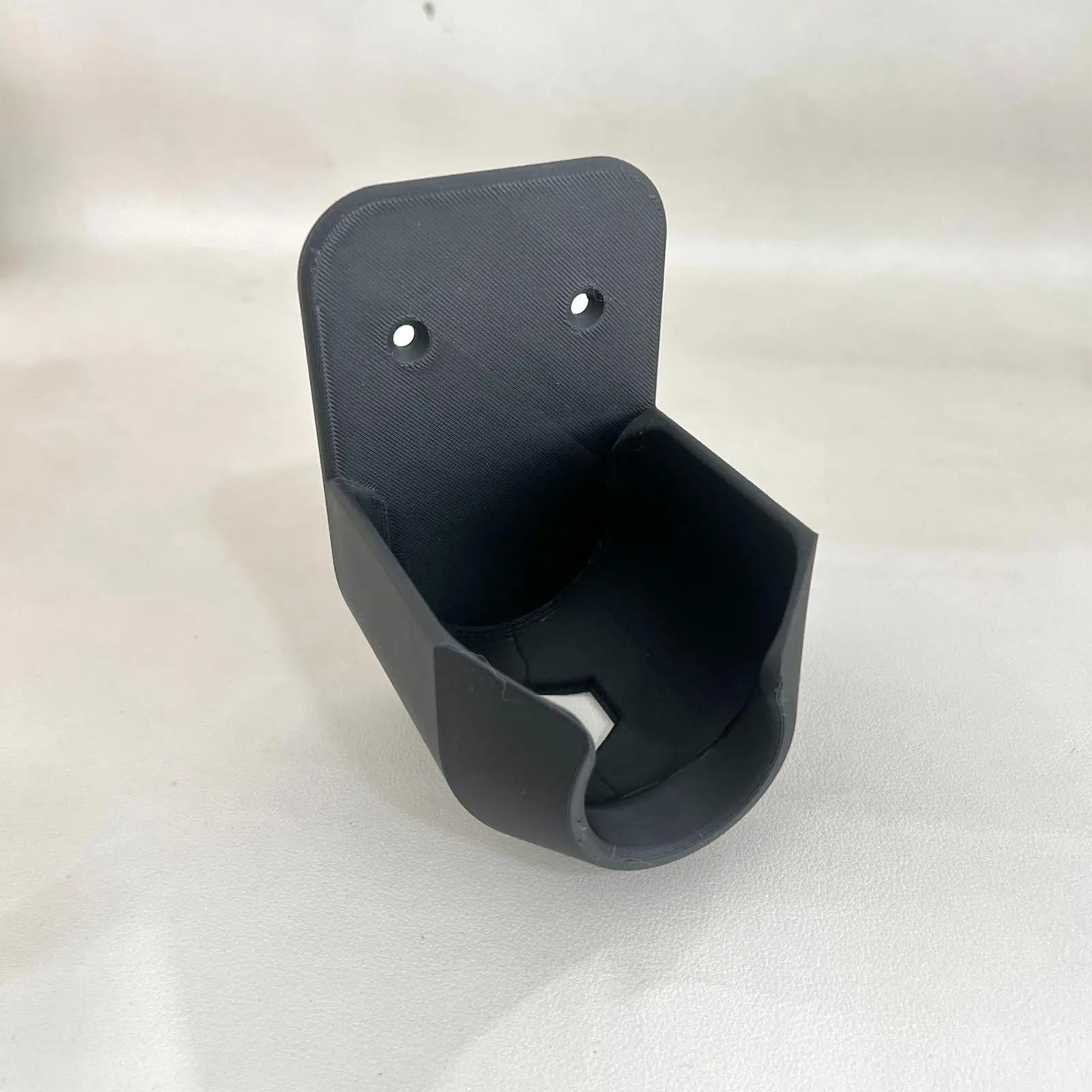 Garden Hose Nozzle Holder in black from an angled view showing the open cradle and drainage cutout