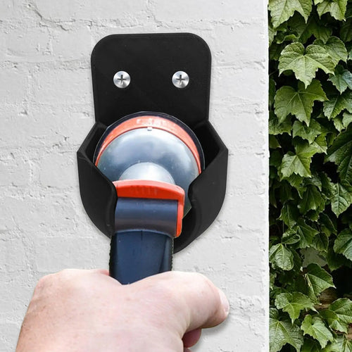 Garden Hose Nozzle Holder mounted on an exterior wall as a spray nozzle is placed into the cradle