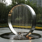Garden Ring Waterfall Fountain with a silver circular frame and water streams above a round pool beside yellow flowers