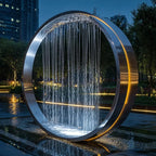 Garden Ring Waterfall Fountain in an evening garden, with water falling through a silver ring into a reflective pool