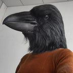 Giant Crow Head Mask worn with an orange sweater, shown in left profile with its long black beak.