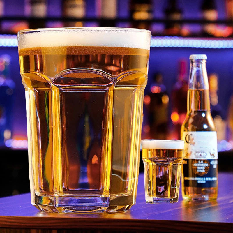Giant Glass Drinking Cup oversized and small filled glasses beside a bottle in a colorful bar scene.