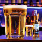 Giant Glass Drinking Cup large filled tumbler beside a smaller glass and bottle on a purple-lit bar.