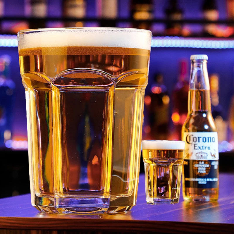 Giant Glass Drinking Cup large filled tumbler beside a smaller glass and bottle on a purple-lit bar.