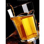 Giant Glass Drinking Cup amber drink being poured into the tilted clear tumbler against a dark background.