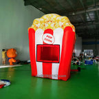 Angled front view of the red and white inflatable popcorn stand with an open serving window and popcorn-print top.
