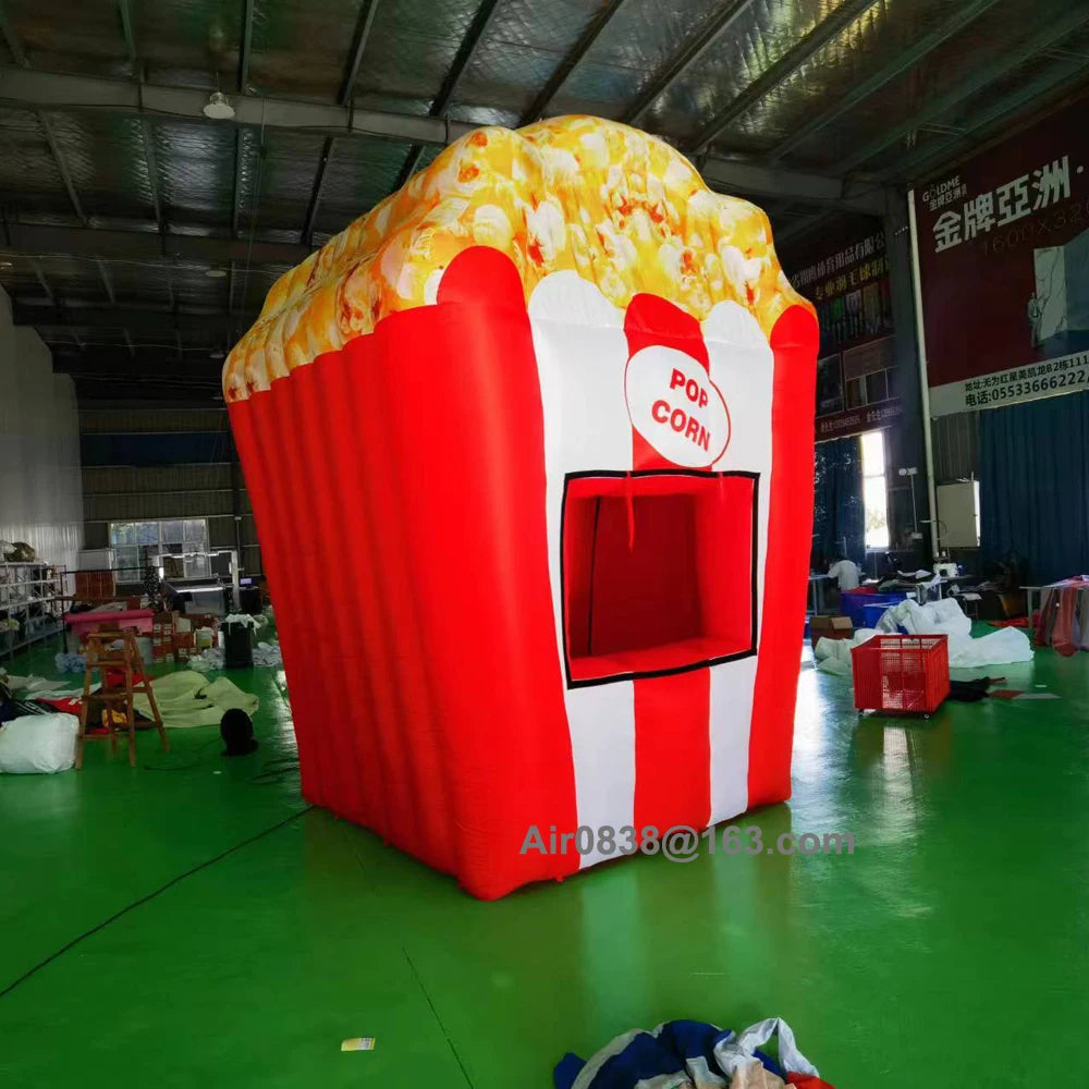 Angled view of the inflatable popcorn stand showing its red side wall, striped front and popcorn-print top.